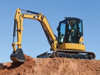 excavator in use at top of dirt mound with blue sky background