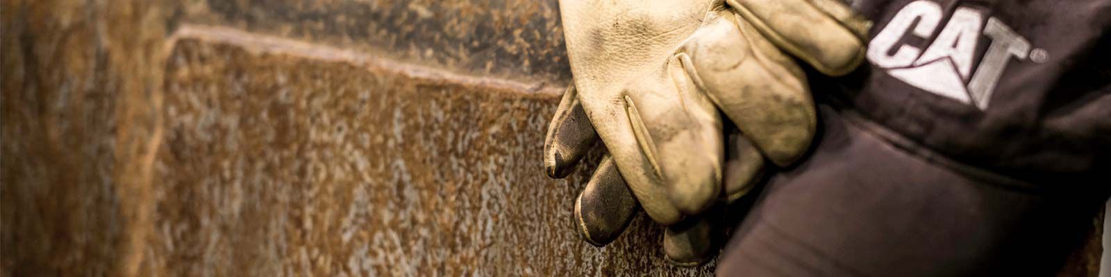 close up of worn out yellow gloves and black CAT ball cap laying on concrete surface