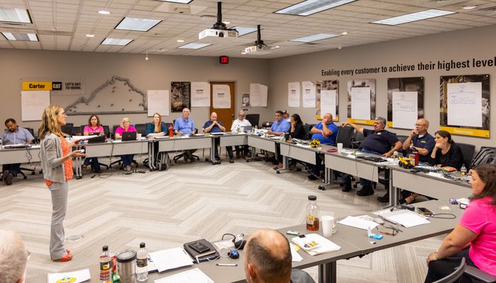 A Carter Cat employee standing up in front of other Carter Cat employees who are seated around her listening to her speak