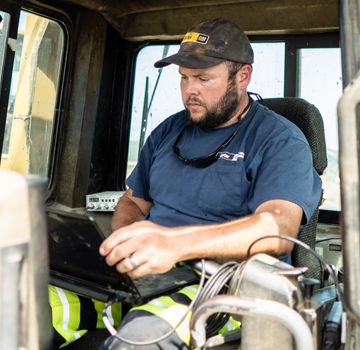 A Carter Cat employee sitting inside a Cat machine working on a laptop