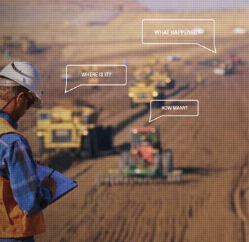 A person writing on a piece of paper in a field with multiple pieces of Cat heavy machinery