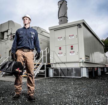 A Carter Cat employee holding a tool bag in front of three electric power generation machines