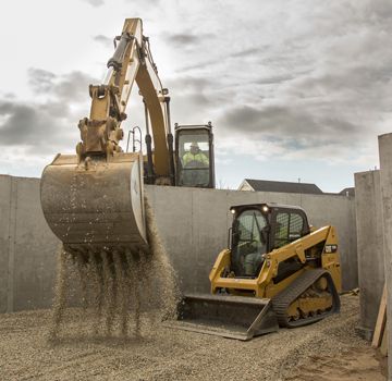 A Cat excavator lifting material and a Cat skid steer