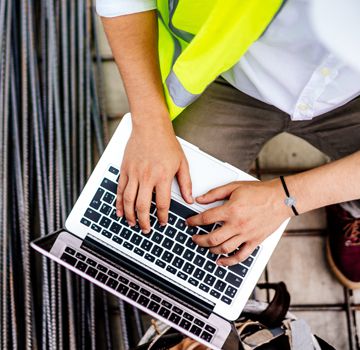 A person wearing a safety vest typing on a laptop