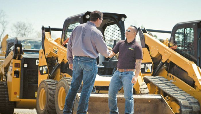 Two men shaking hands in front of 3 different pieces of Cat machinery