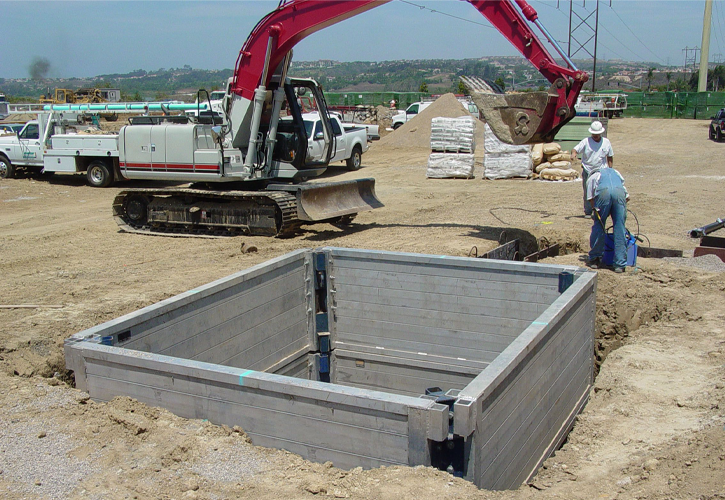 A red excavator lifting material out of trench shoring equipment