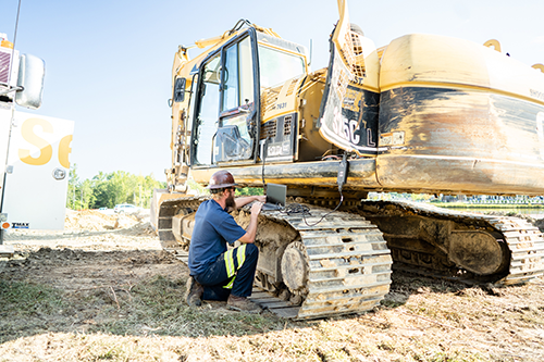 A male Carter Cat field technician working on a mini excavator in the field
